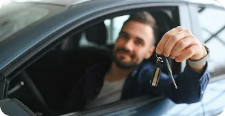 Homem dentro de um carro estende mão pela janela segurando a chave.