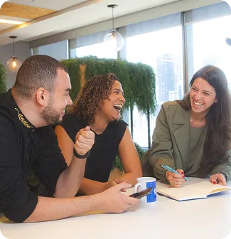 Três pessoas em escritório conversam e anotam ideias à mesa.
