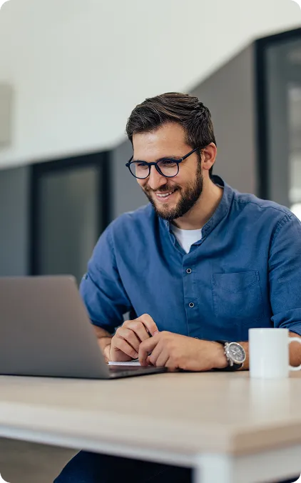 Homem usando laptop em mesa, com caneca ao lado em ambiente moderno.