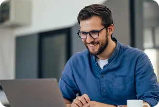 Homem usando laptop em mesa, com caneca ao lado em ambiente moderno.