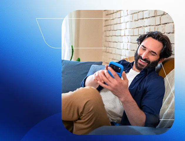 Um homem sorri enquanto usa o celular sentado no sofá.
