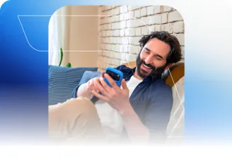 Um homem sorri enquanto usa o celular sentado no sofá.