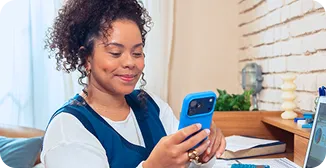 Uma mulher está sorrindo enquanto olha o celular e o segura com uma das mãos.