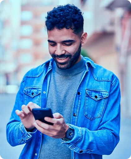 Um homem de jaqueta azul, segura o celular com as duas mãos, olha para a tela e sorri.