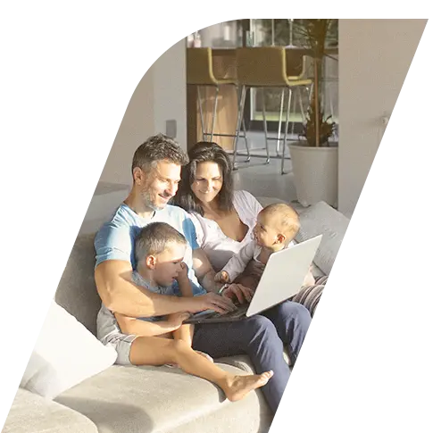 Família com pai, mãe e duas crianças pequenas no sofá sorrindo e utilizando um computador portátil