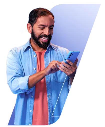 Um homem branco, com cabelo castanho escuro e barba, ambos de tamanho curto, está usando uma camiseta laranja com uma jaqueta jeans por cima. Ele está sorrindo enquanto mexe no celular, segurando com as duas mãos.
