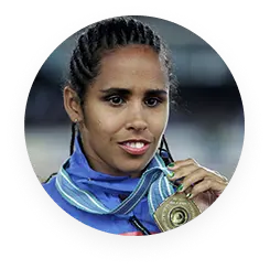 Uma foto da ex-ginasta Ádria Santos. Ela está sorrindo, com uniforme azul e segurando para a câmera uma medalha de ouro pendurada em seu peito.