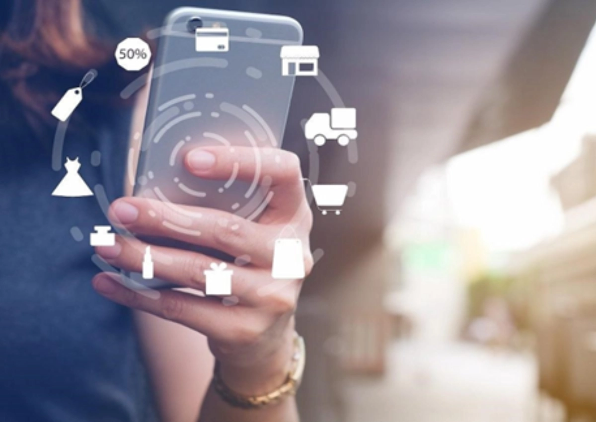 Mulher com celular em mãos vendo sobre o iniciador de pagamentos. Há vários ícones de compras na frente da tela do celular.