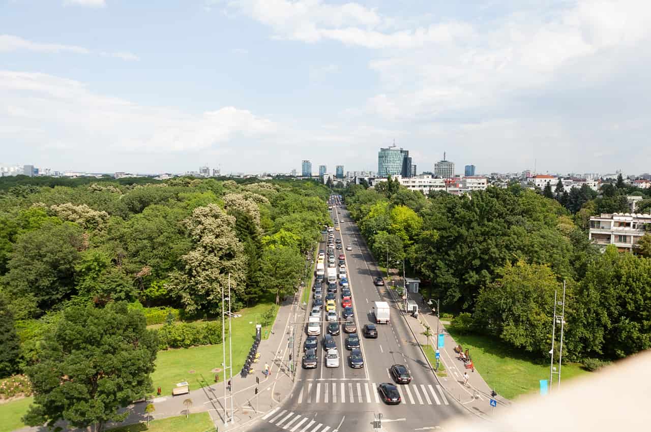 Vista aérea de uma avenida movimentada com carros no trânsito cercada por árvores.