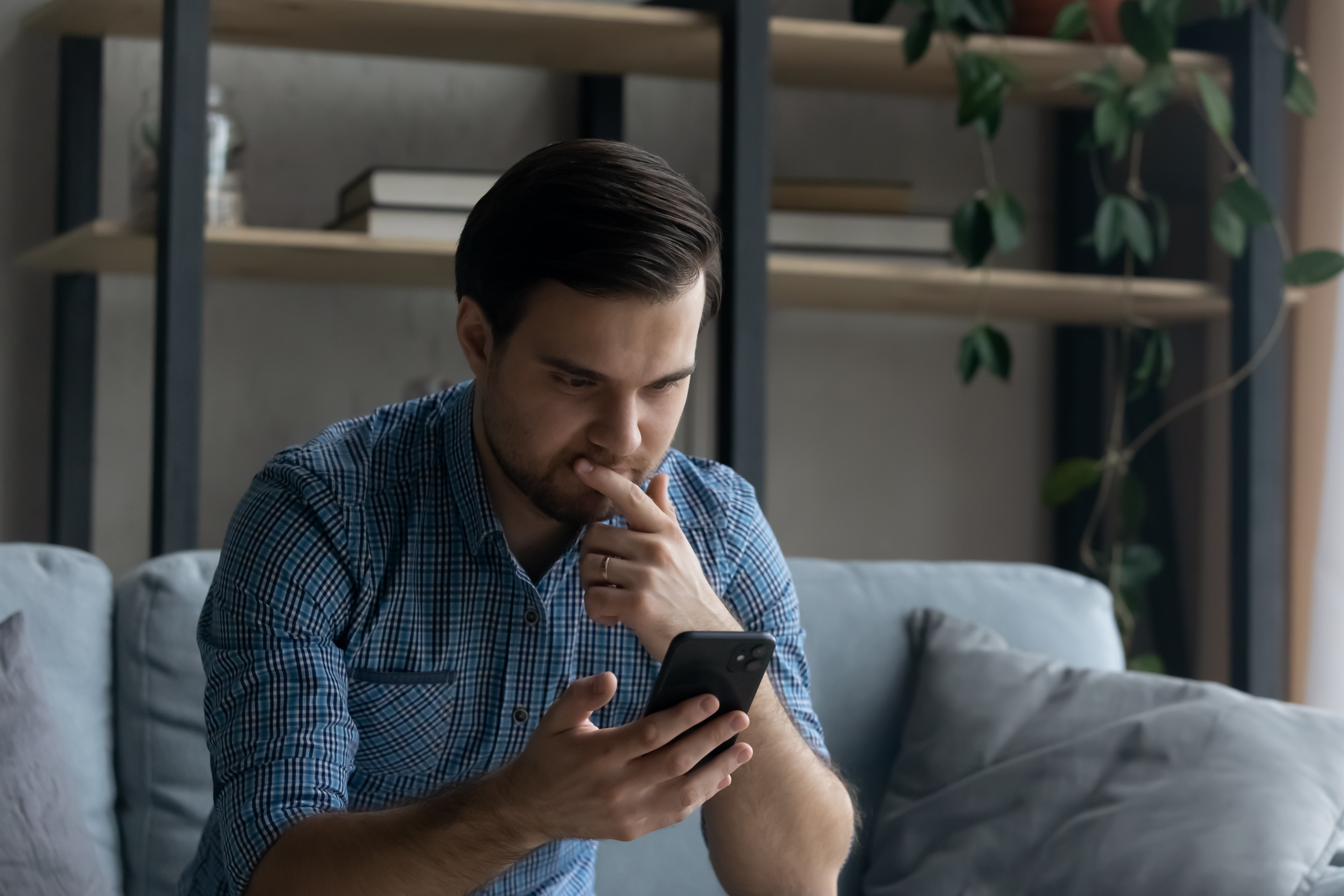 homem sentando no sofá com o celular em uma das mãos pensativo