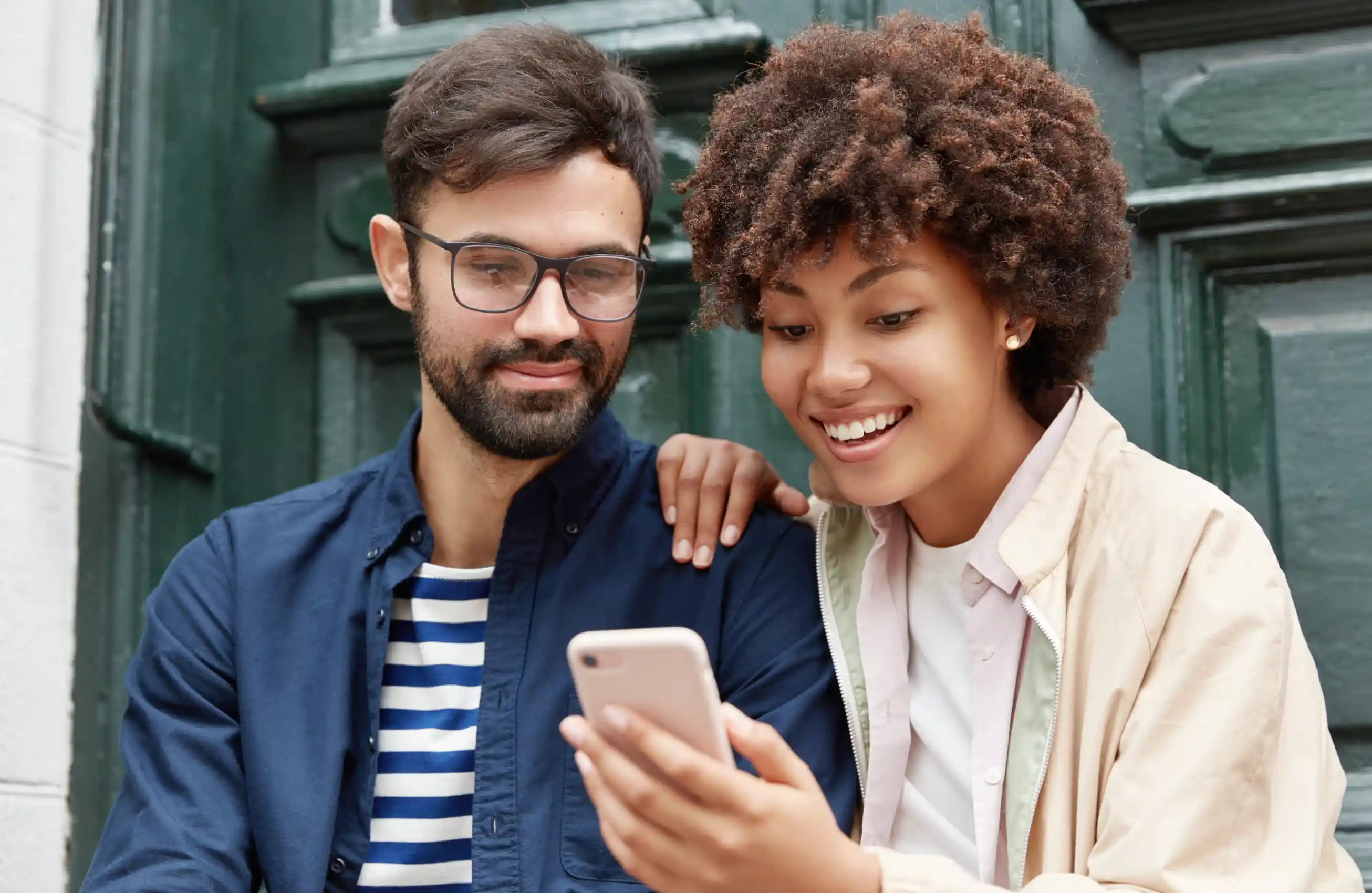 Um casal encarando um smartphone na frente de uma casa.
