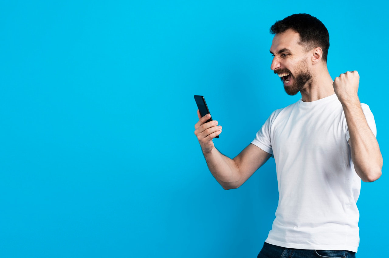 Homem feliz segurando o celular, fazendo um gesto de celebração de uma conquista.