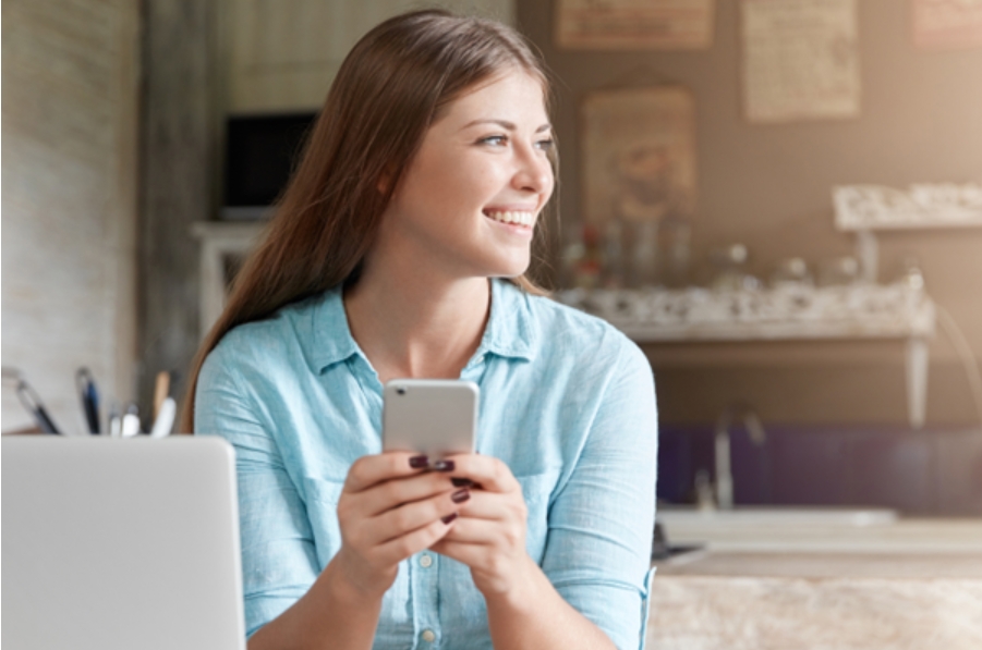 Mulher sorrindo com celular em mãos, pensando que vale a pena compartilhar dados entre bancos.