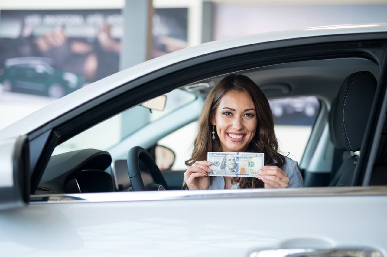 Mulher sorrindo e segurando nota de dinheiro dentro de veículo após ter um carro 100% financiado.