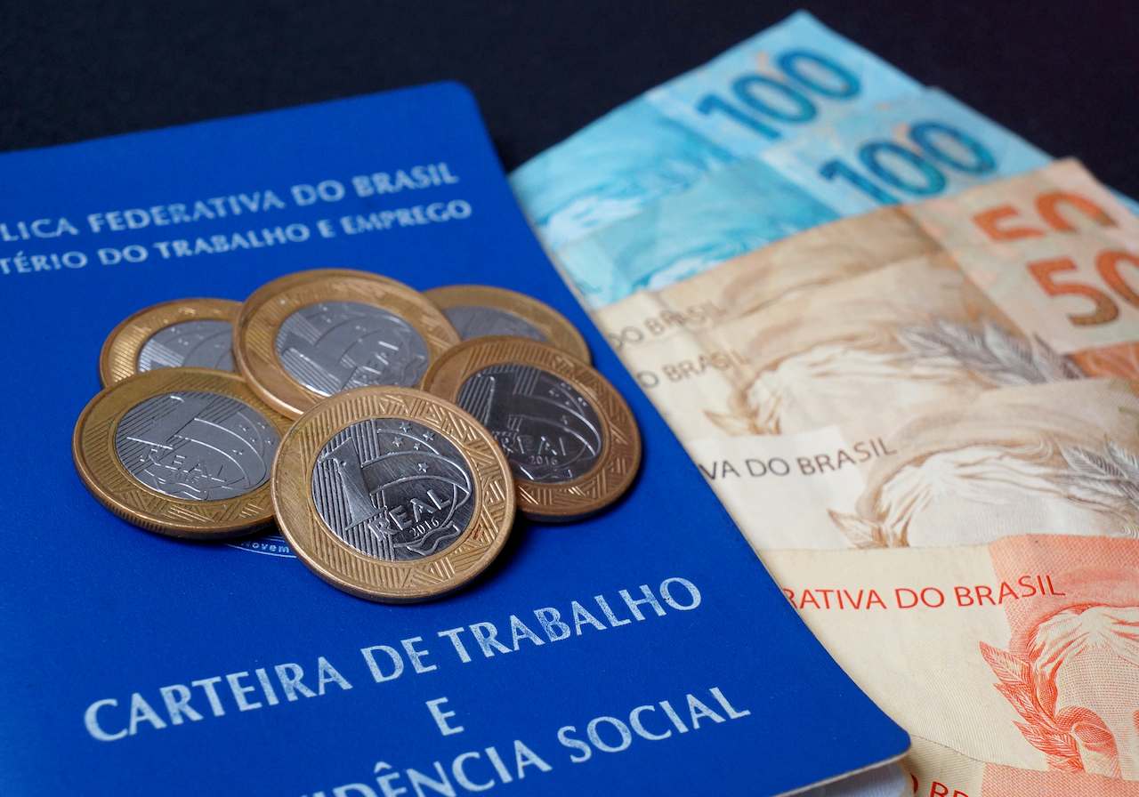 Carteira de Trabalho e Emprego coberta por moedas de R$1 (Real) e notas de r$100,00.