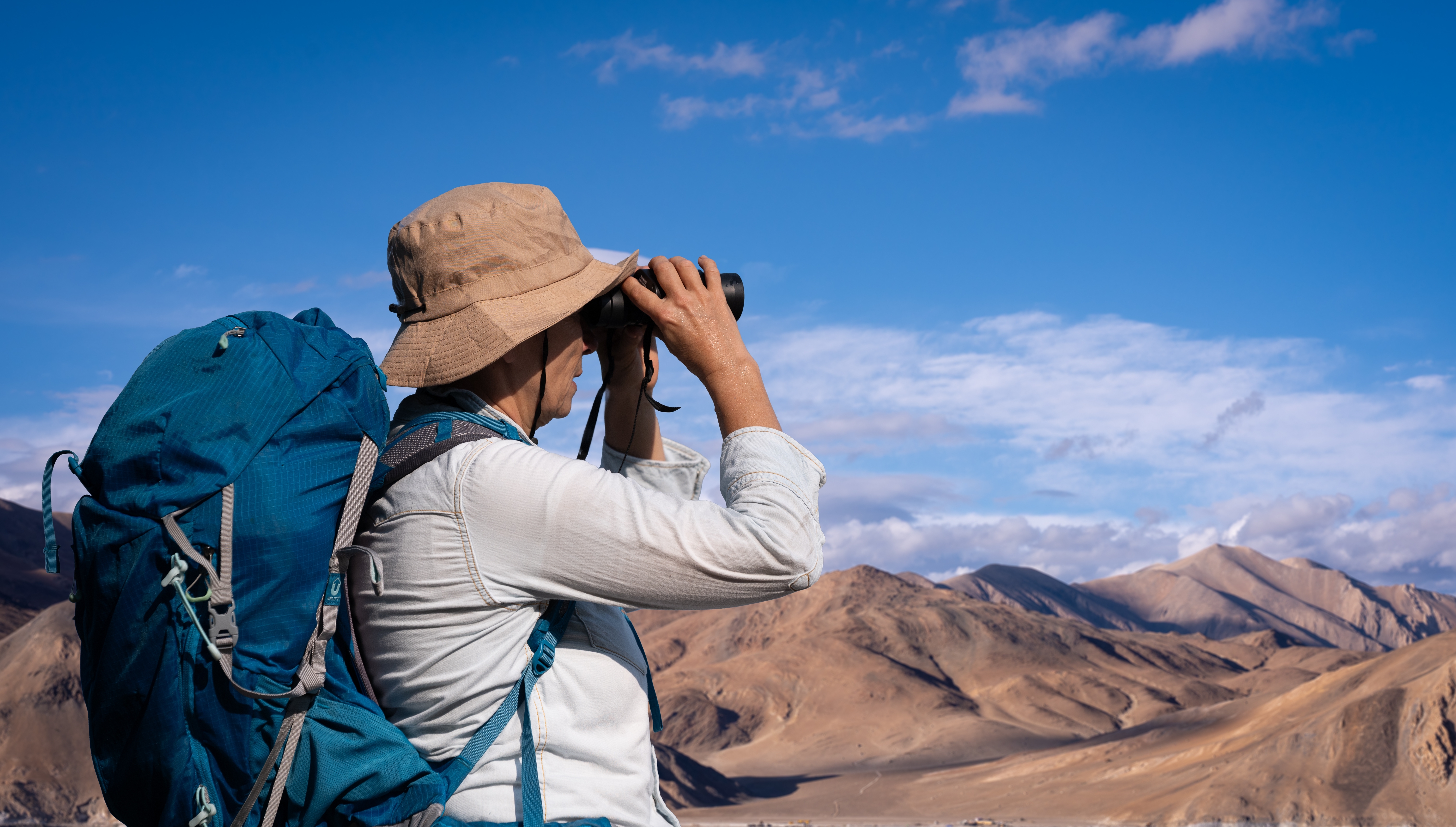 homem com mochila nas costas, avistando paisagem nas montanhas com binóculos 