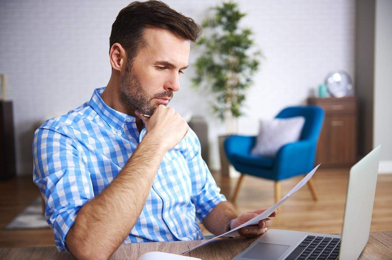 Homem com expressão concentrada, apoiando a mão direita no queixo e segurando folhas de papel.