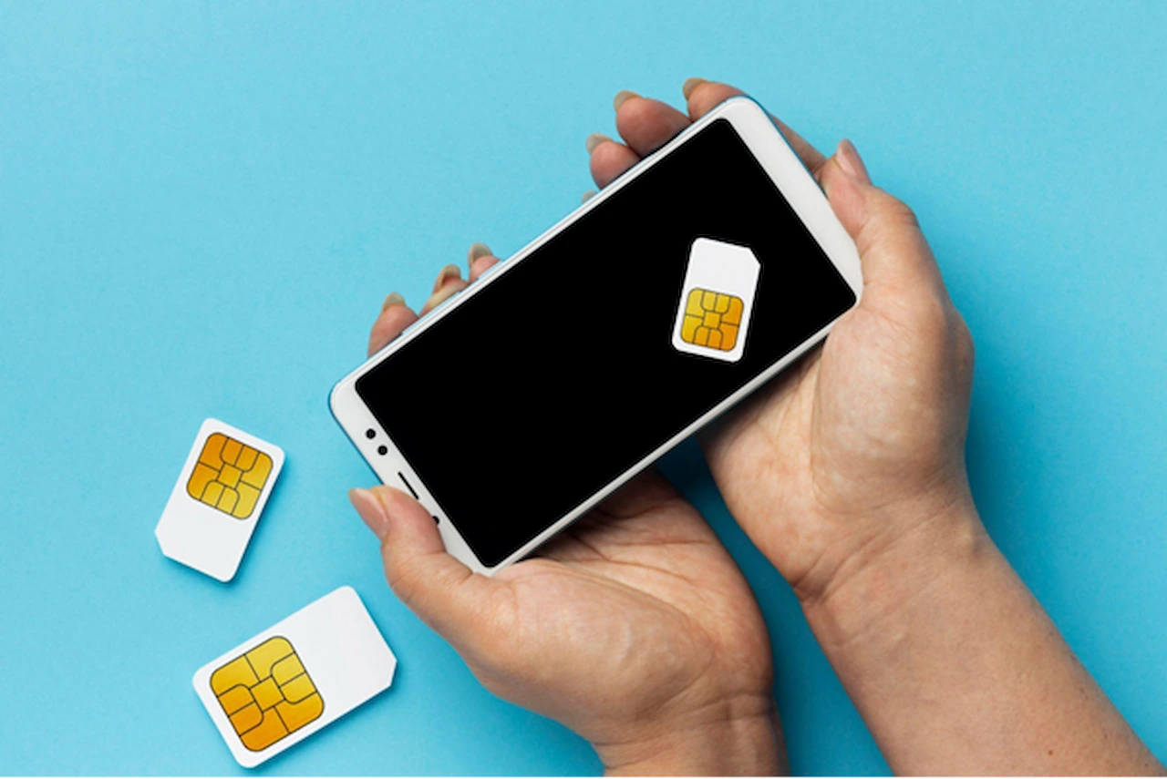 Duas mãos segurando um celular com um chip em cima, e dois chips de celulares apoiados ao lado.