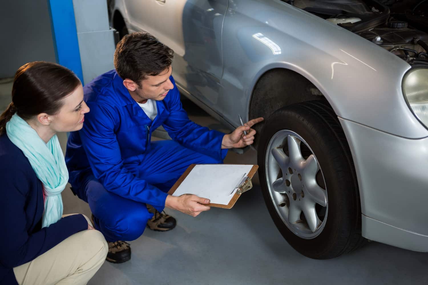 Mecânico e mulher analisando o pneu de um carro usado, em vistoria veicular.
