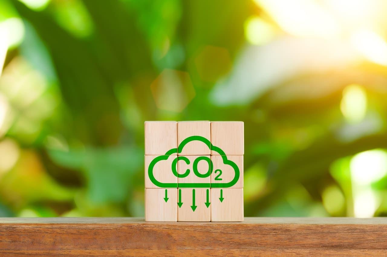 Bloco de madeira com símbolo de CO2 e setas apontando para baixo, representando a redução de emissões.