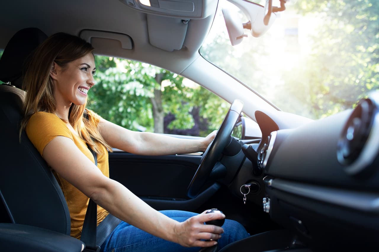 Mulher sorridente dentro de um carro automático, pronta para dirigir.