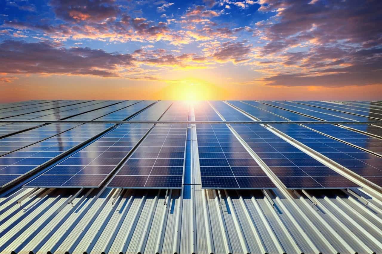 Painéis solares em telhado metálico com pôr do sol ao fundo.