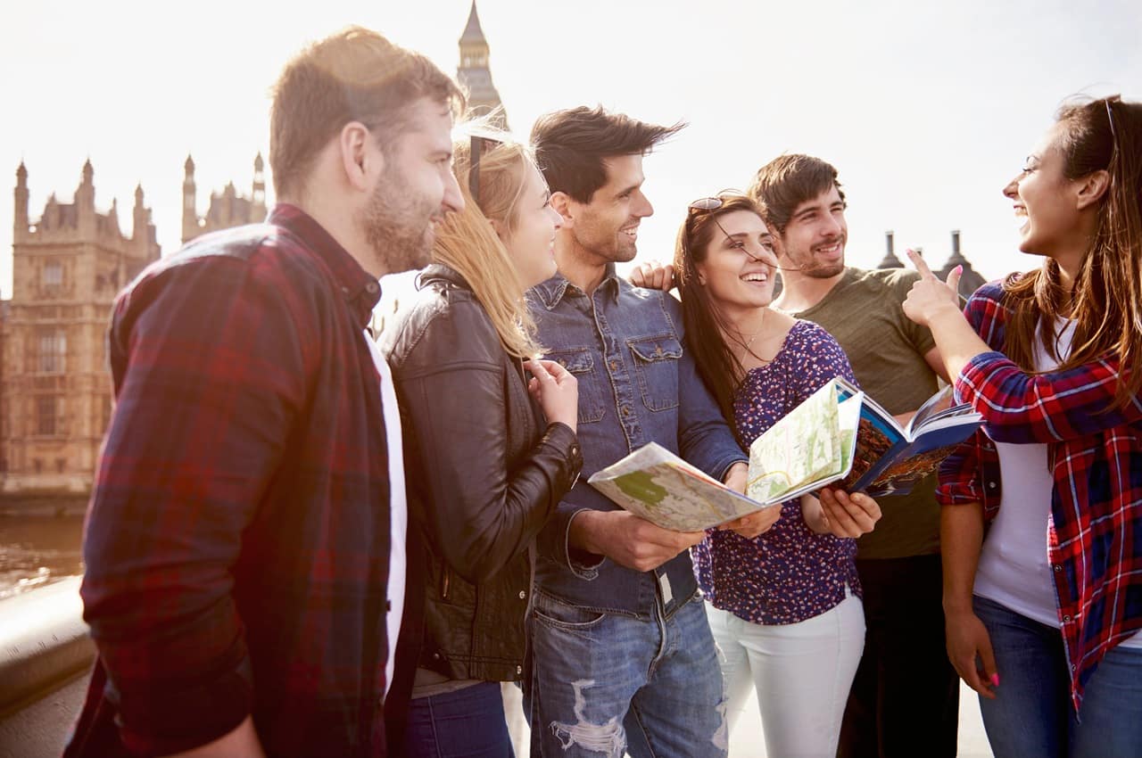 Grupo de seis amigos intercambistas ao ar livre, sorrindo e segurando mapas de papel.