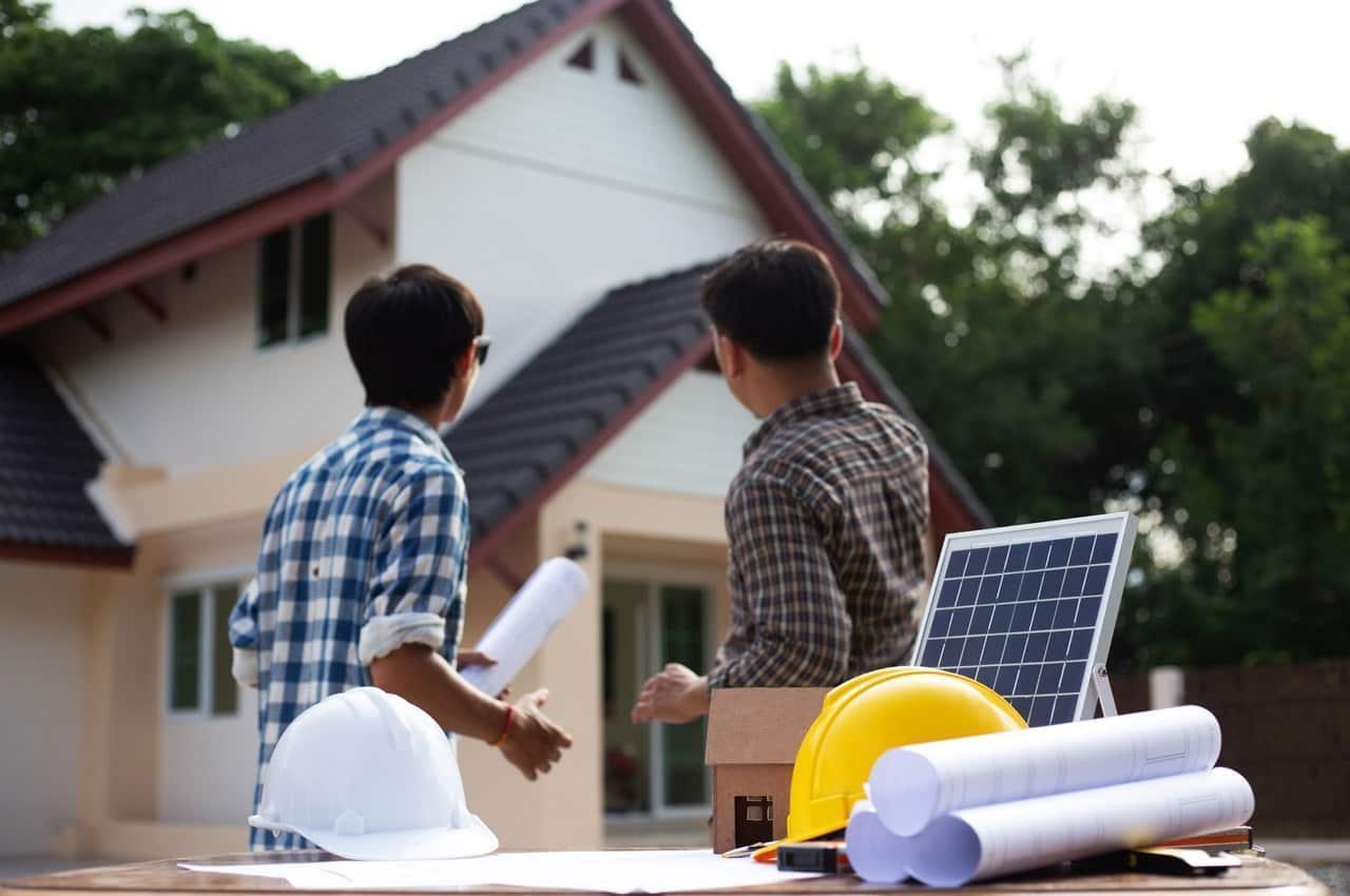Dois técnicos analisando projetos de instalação de energia solar em frente a uma residência.