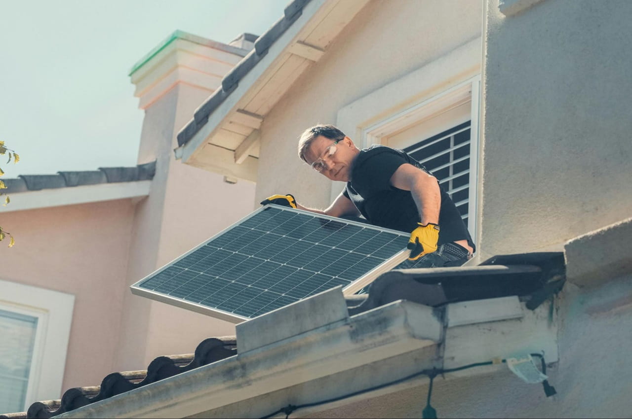 Homem instalando painel solar no telhado de uma casa.