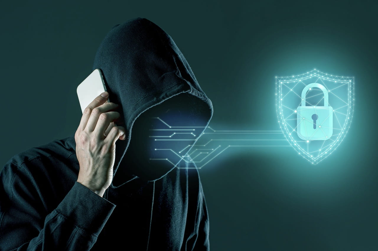 Homem de capuz com o rosto oculto falando ao celular enquanto aplica o golpe do falso advogado. Ao seu lado, há o holograma de um gráfico digital brilhante de um escudo com cadeado.