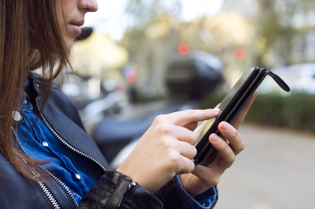 Mulher de perfil digitando na tela do celular para consultar como pagar uma multa de trânsito.
