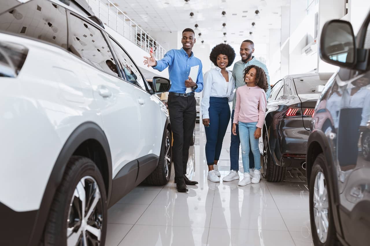 Homem, mulher e filha em uma concessionária conversando com um vendedor entre dois carros