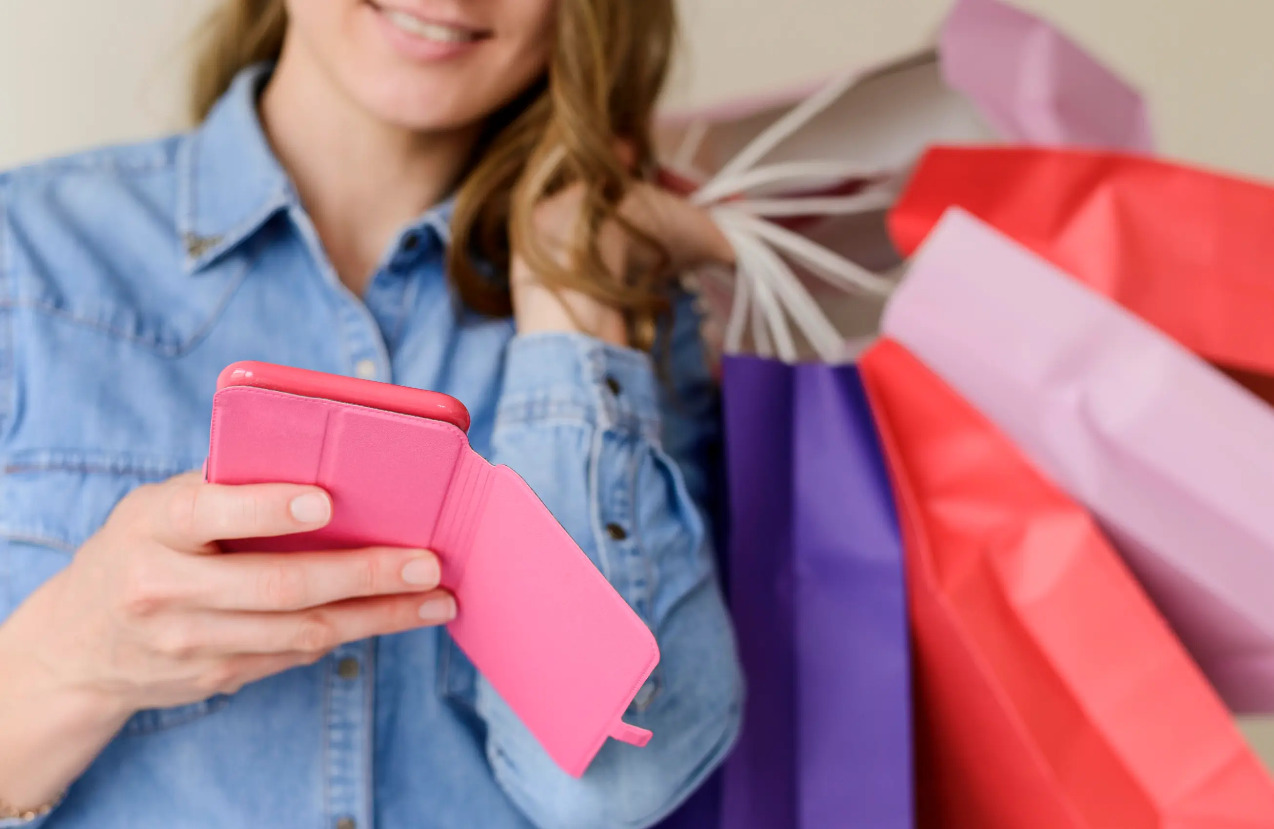 Mulher sorrindo sentada no sofá com várias sacolas de compras coloridas ao redor, segurando um cartão de crédito na mão direita e usando um laptop apoiado no colo. 
