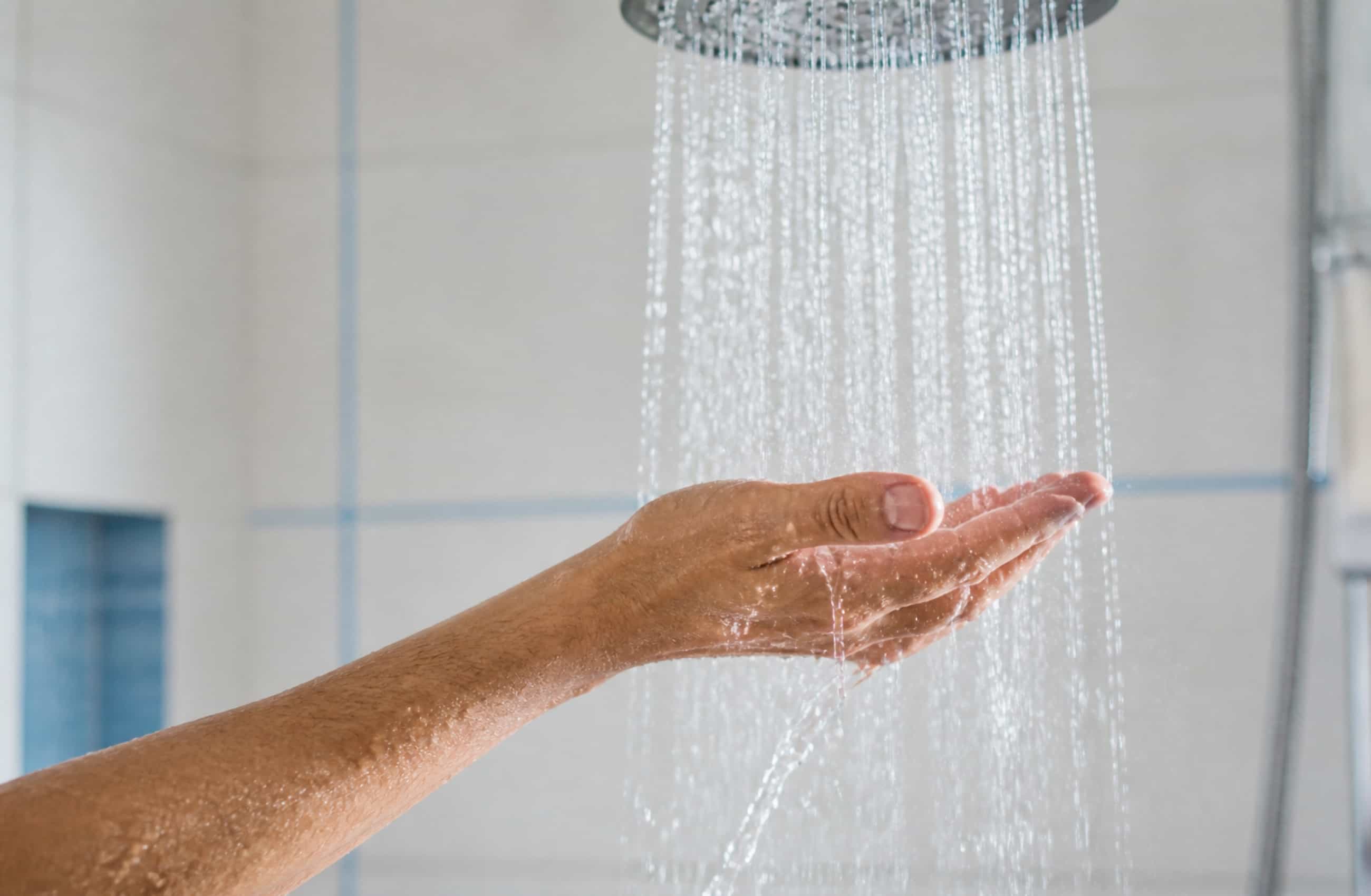 Uma mão adulta testando a temperatura da água do chuveiro. 