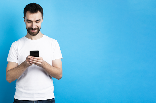 Um homem utilizando um smartphone em um fundo azul.
