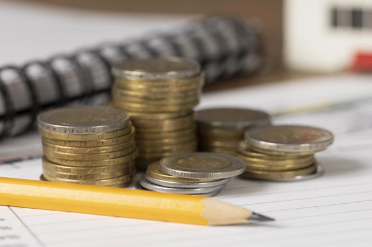 Moedas douradas, com lápis de escrever na frente e caderno de notas no fundo.