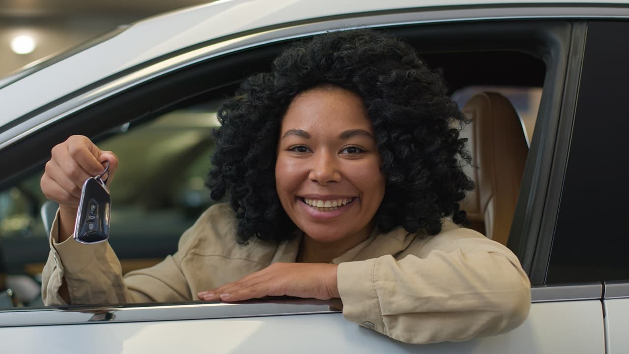 mulher sorrindo, dentro do carro, segurando chave do carro 