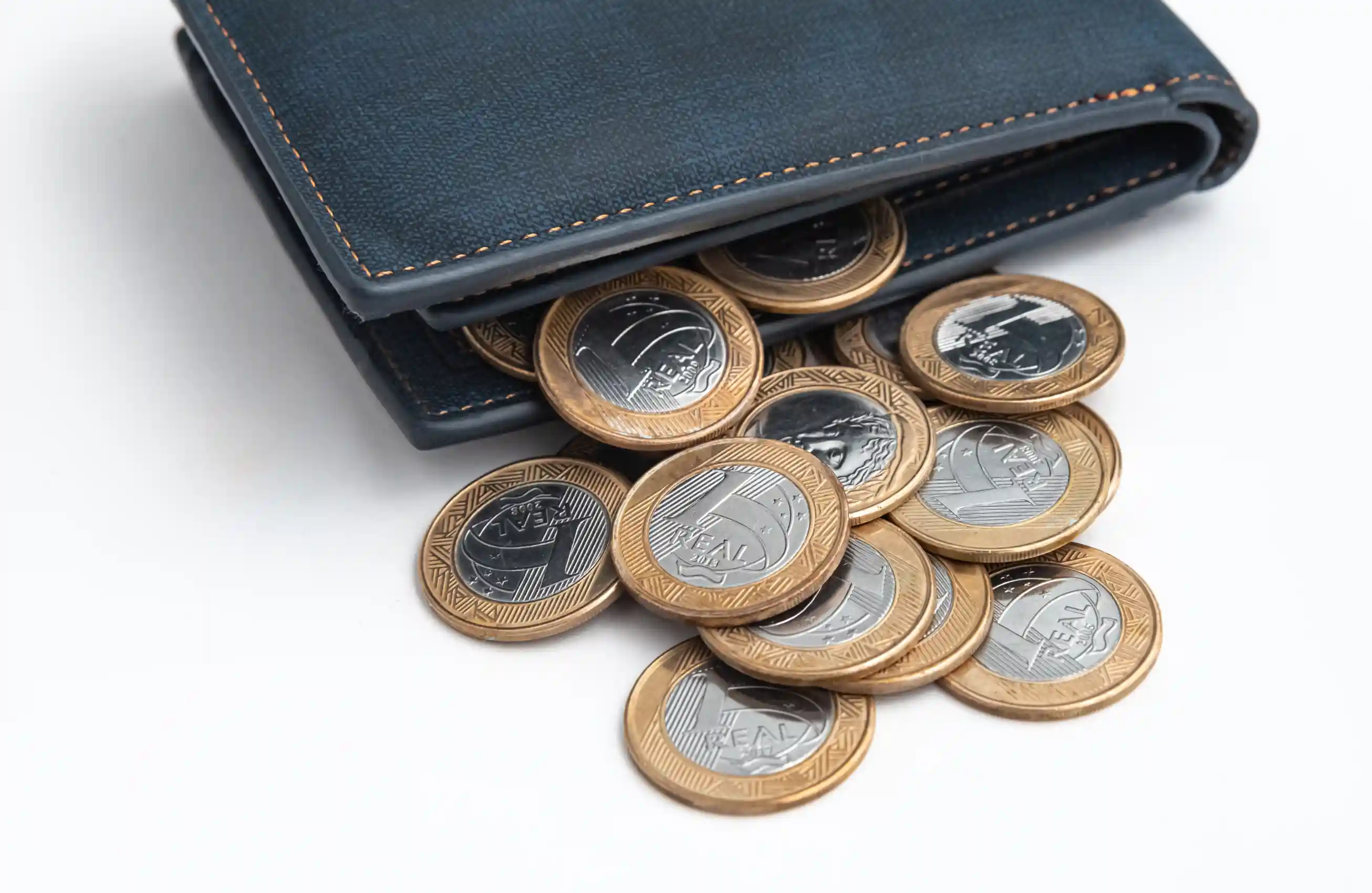 Uma carteira aberta sobre uma mesa branca, com moedas caindo na mesa.