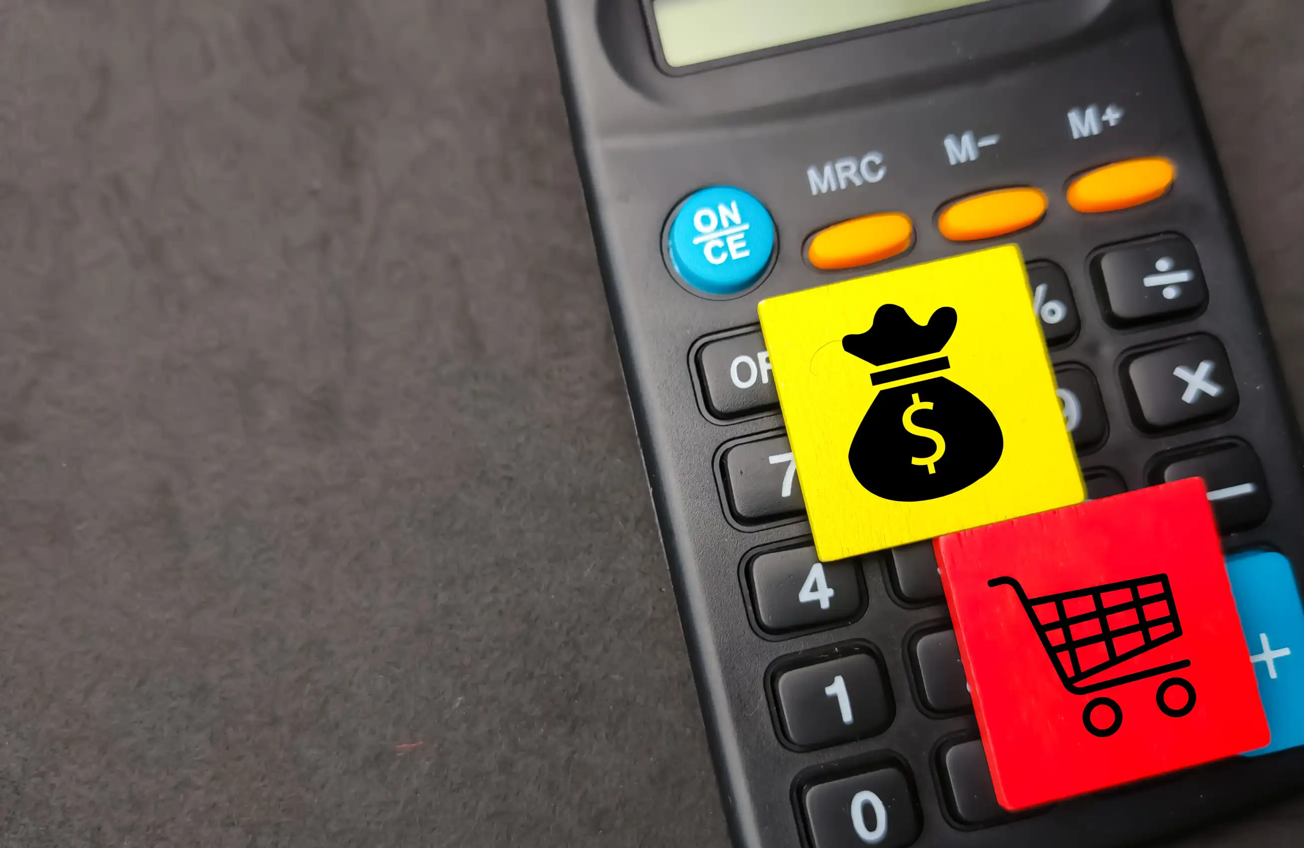 Calculadora com adesivos amarelo (saco de dinheiro) e vermelho (carrinho de compras) colados sobre os botões, sugerindo transação financeira. 