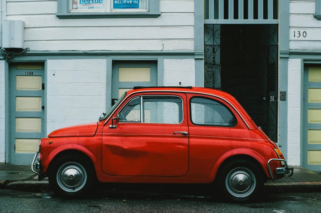 Carro vermelho estacionado na rua, com a lateral amassada.