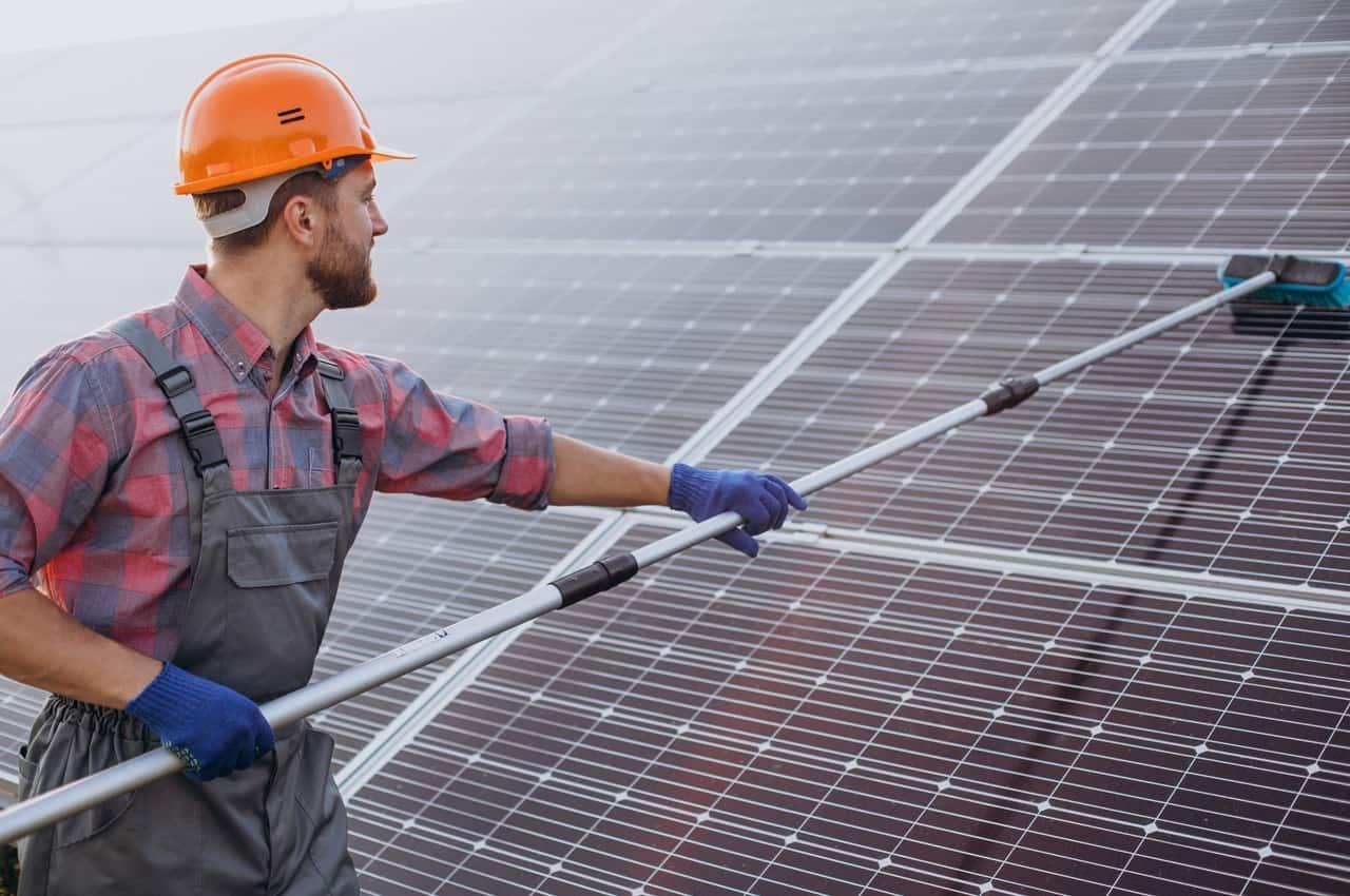 Homem fazendo a limpeza de painéis solares. Ele usa equipamentos de segurança.