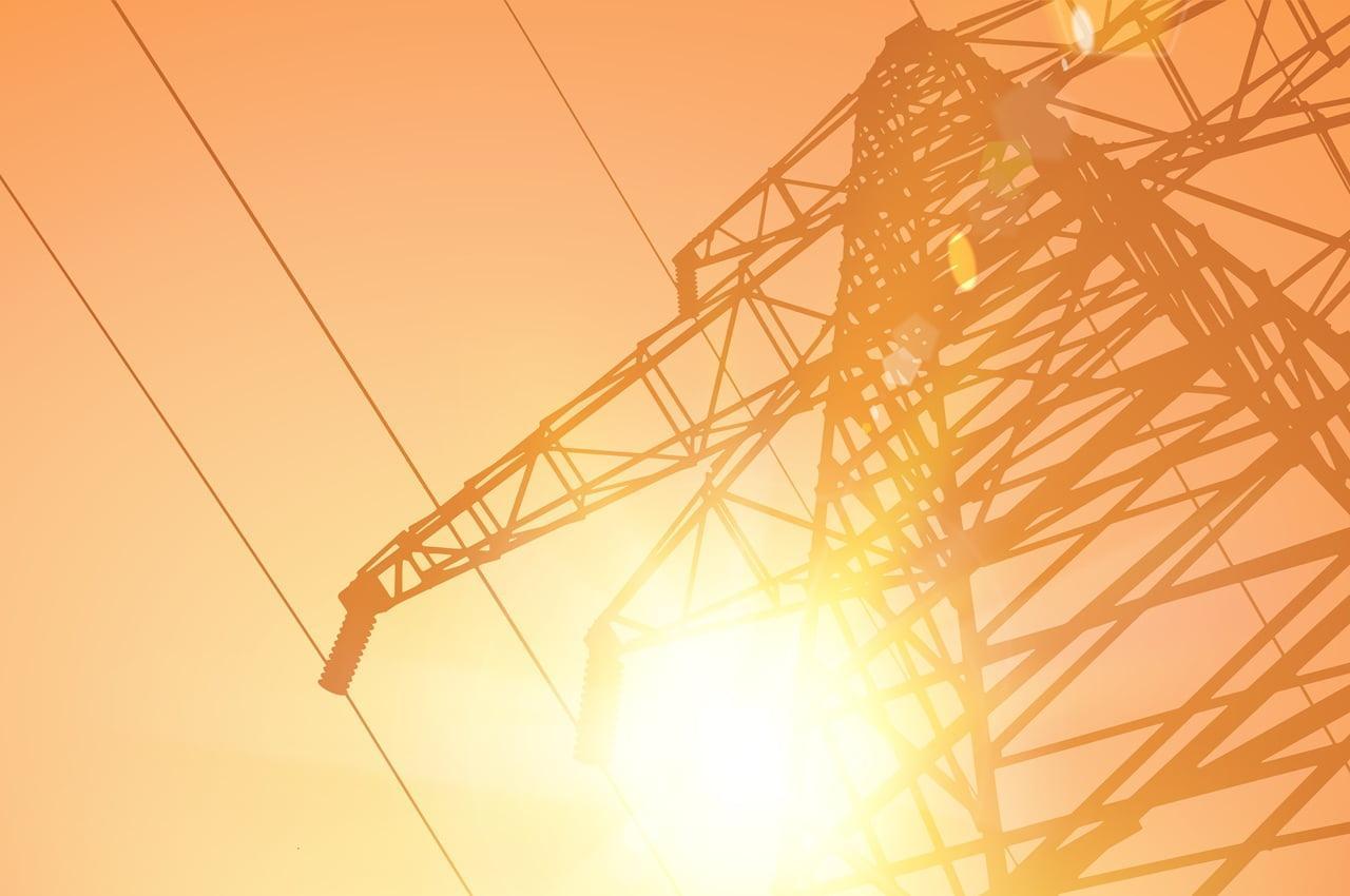 Estrutura de uma torre de transmissão de energia ao pôr do sol, com raios solares refletindo.