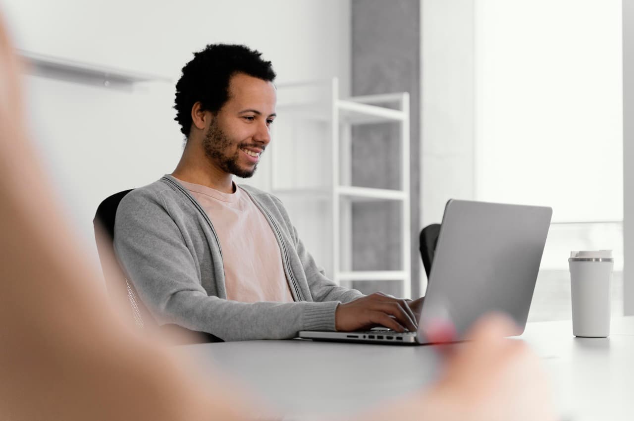 Homem sorrindo e digitando em notebook, em um escritório, para representar a busca pelo Empréstimo com Garantia de Veículo BV.