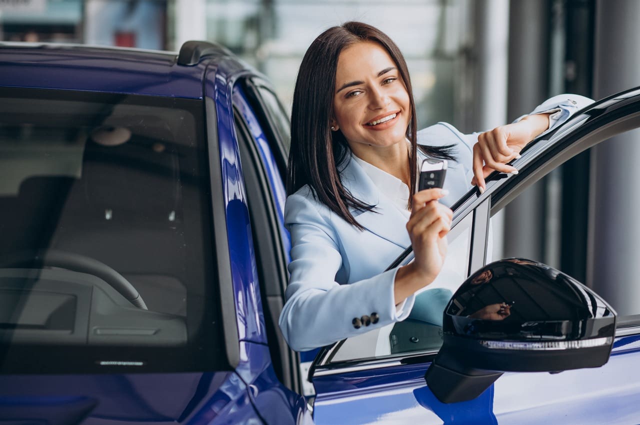 Mulher sorridente, ao lado de um carro azul, segurando a chave do automóvel. Ela está feliz com o seu empréstimo com garantia de veículo financiado.