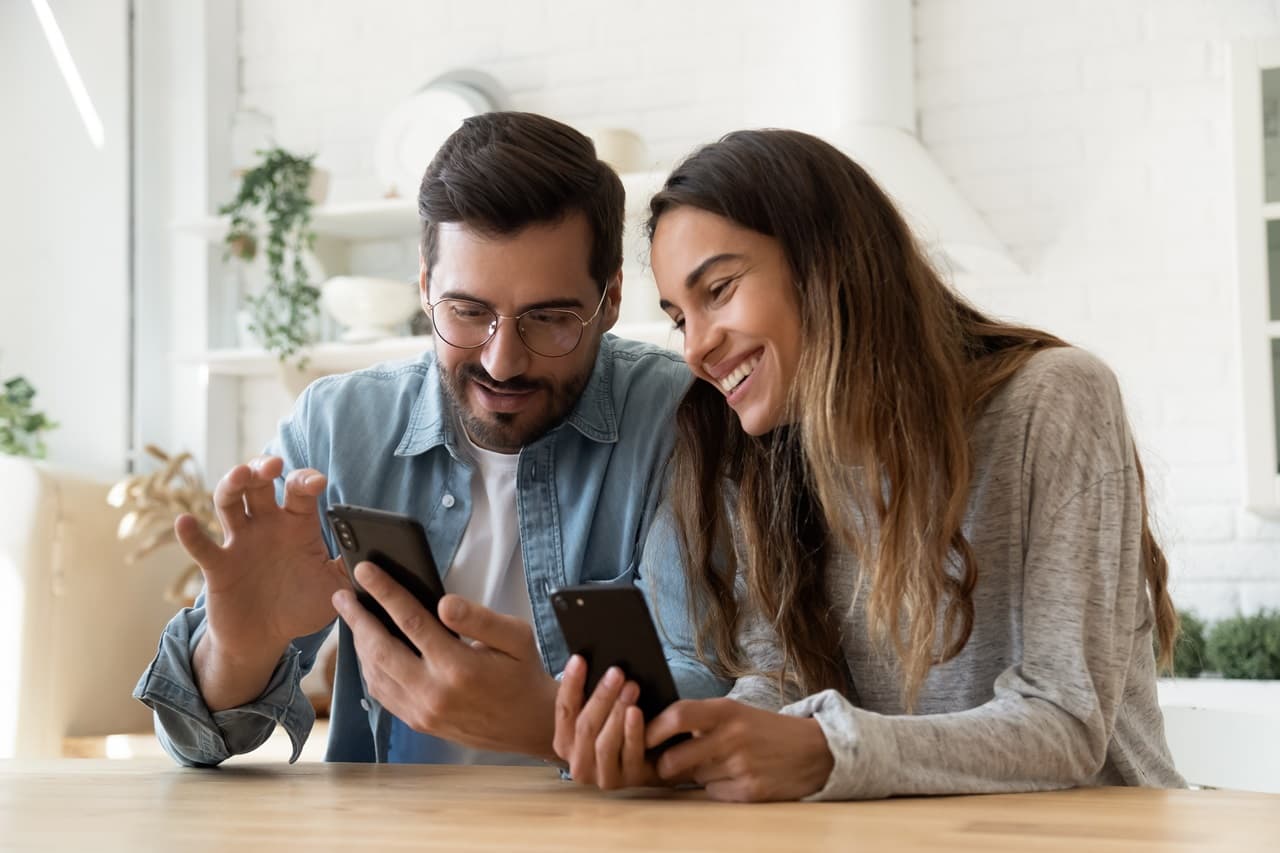 homem e mulher sentados, sorrindo, olhando para celular
