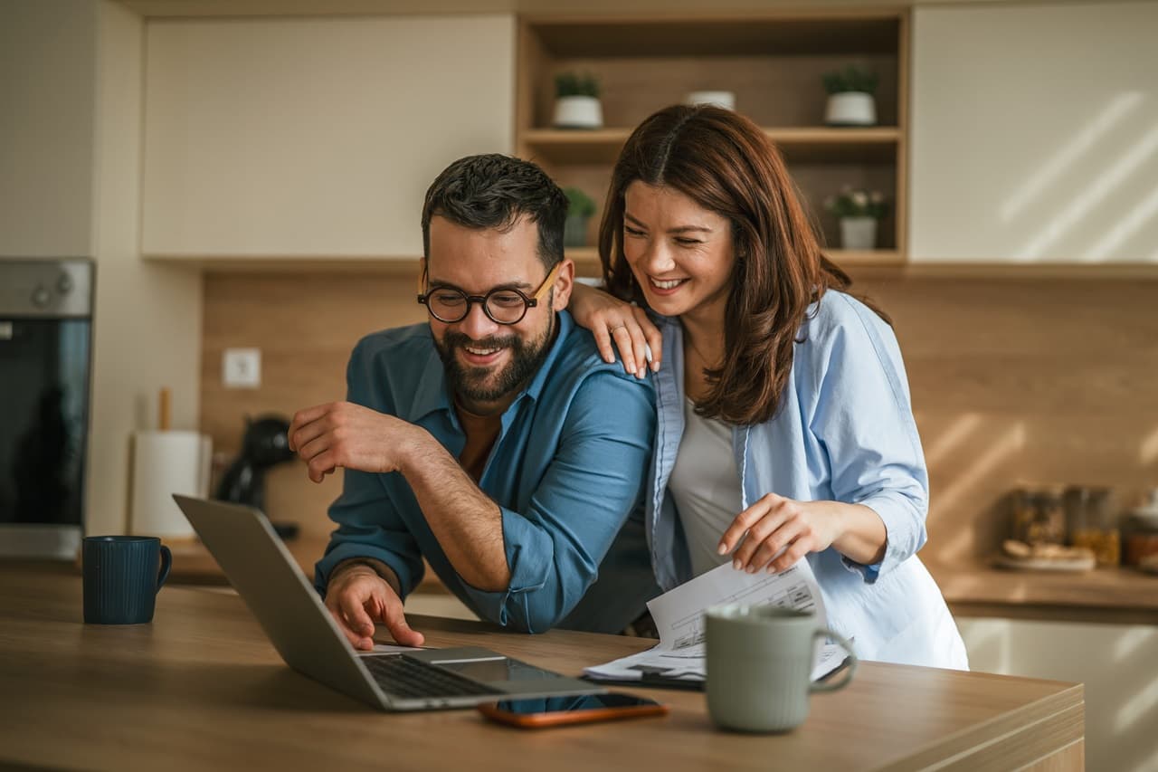 Homem e mulher sorrindo, analisando informações no notebook e papeis.