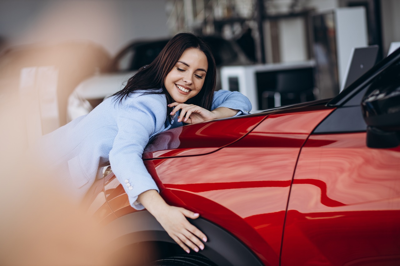 mulher inclinada em frente ao carro vermelho, abraçando a frente do carro