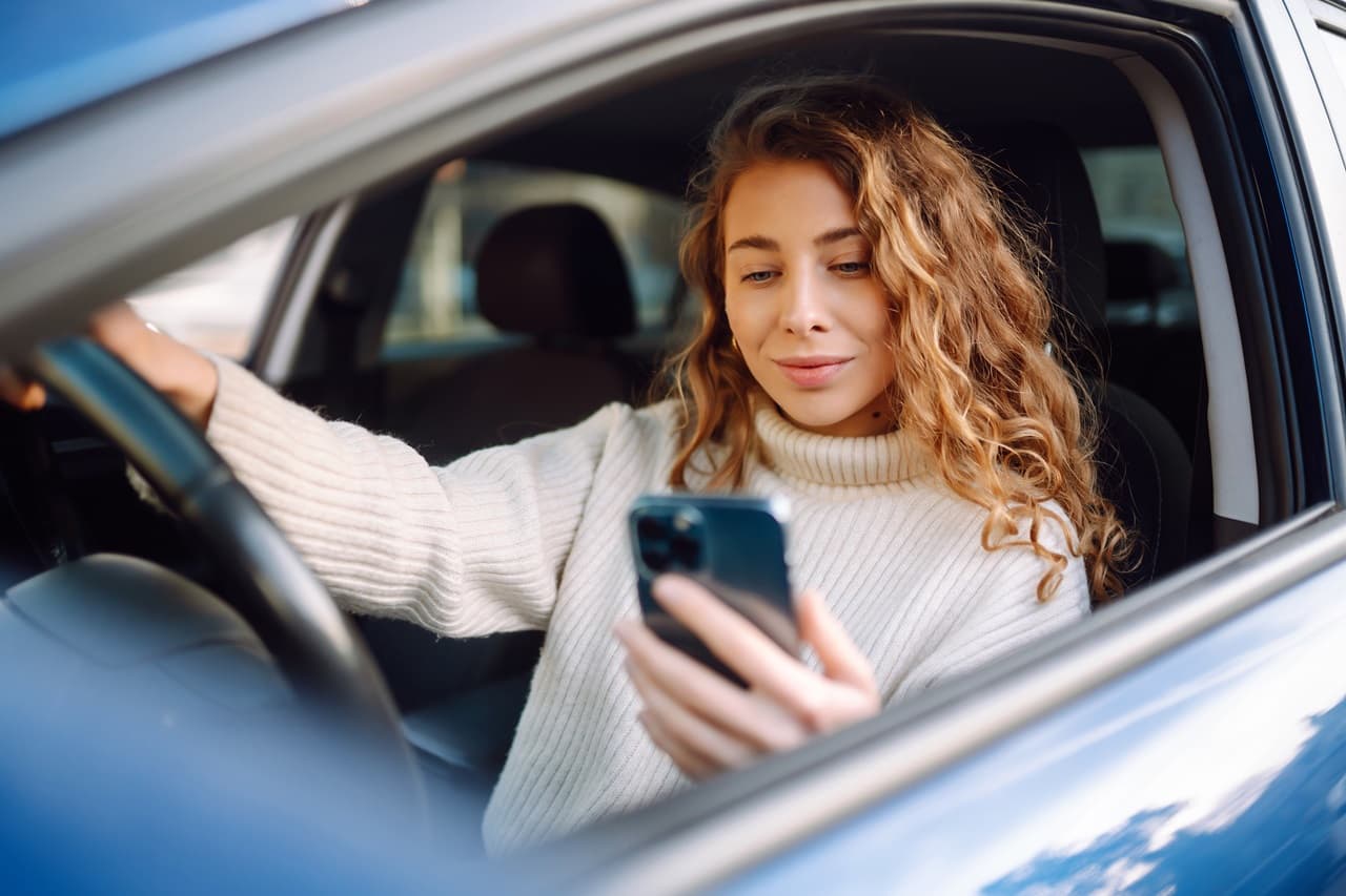 Mulher dentro de um veículo parado, segurando um celular na mão