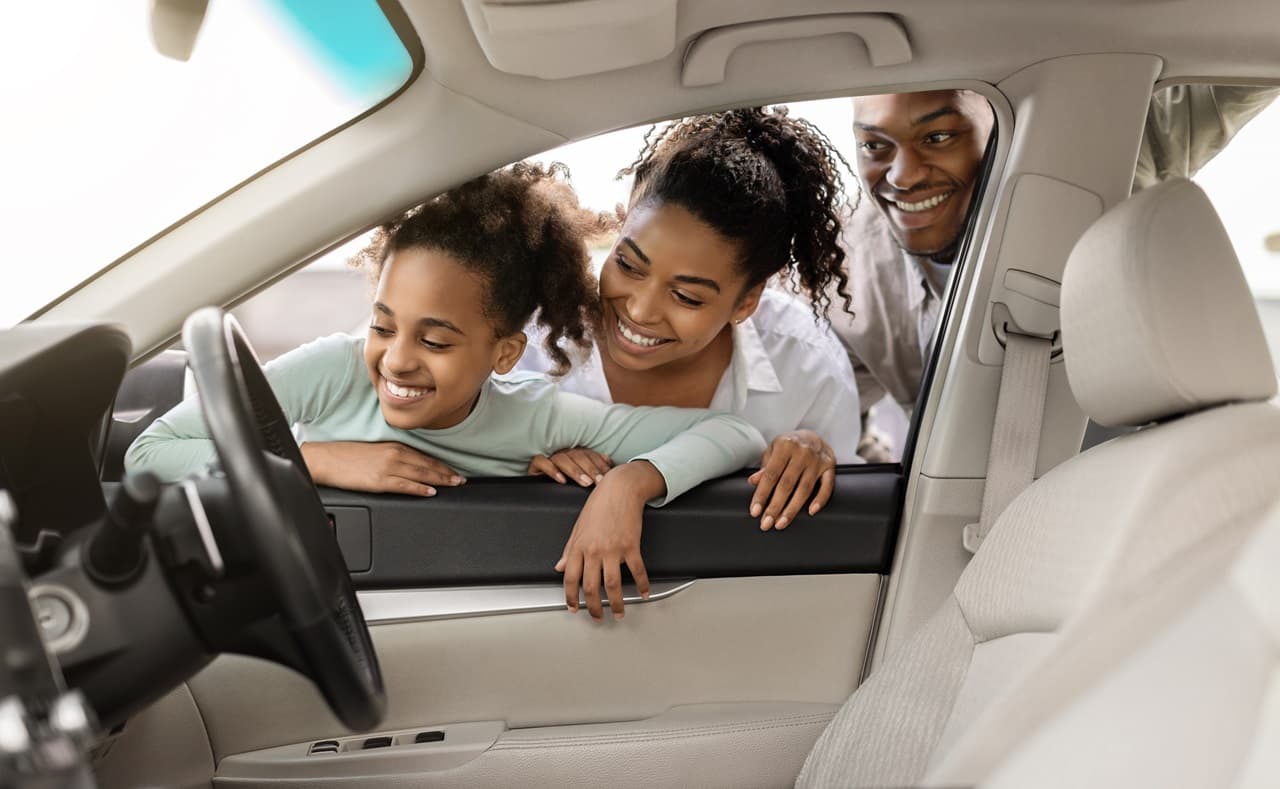 Menina, mulher e homem do lado de fora do carro olhando o painel.
