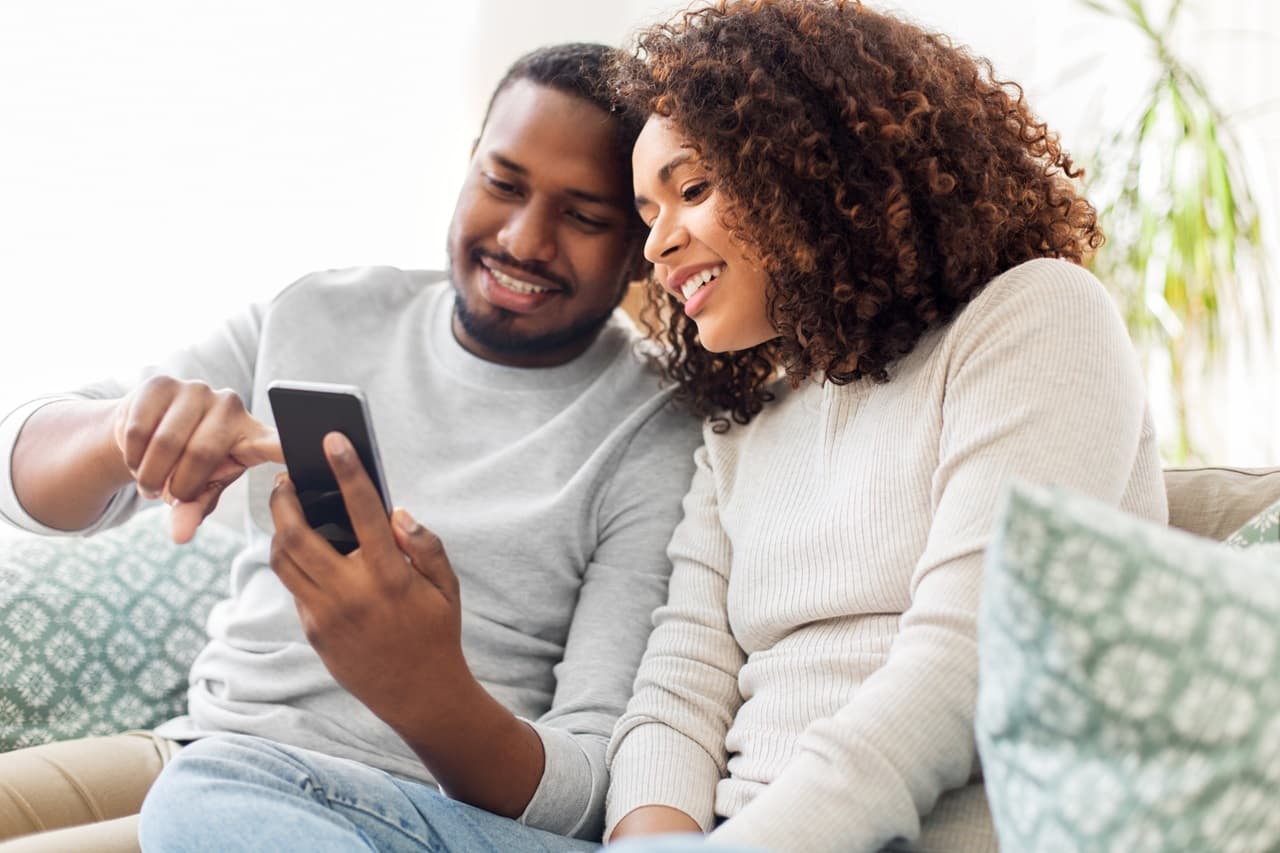 Casal sentado no sofá, olhando para o celular